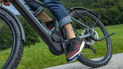 The image shows a close-up of a gray Cube Reaction Hybrid Allroad bike. A closer look at the bottom bracket and motor block of the e-bike while riding.