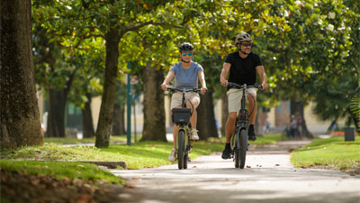A couple rides a Cube folding bike through a park.