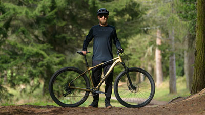 A man can be seen behind his golden Cube mountain bike on a forest path.