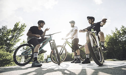 Three freestyle cyclists are standing next to their bikes, chatting on a sunny day.