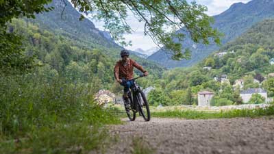 A cyclist rides his mountain bike along a gravel path, with a mountainous landscape in the background.