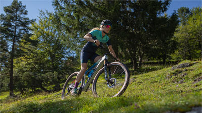 A cyclist can be seen riding her mountain bike. She is riding through steep terrain.