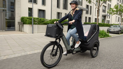 A woman rides a gray cargo bike through a residential area.