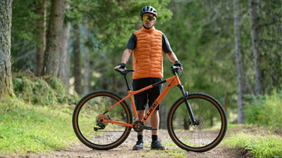 A man stands behind his orange Cube mountain bike on a forest path.