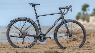 A black Cube gravel bike can be seen standing on rocky terrain with the coast in the background.