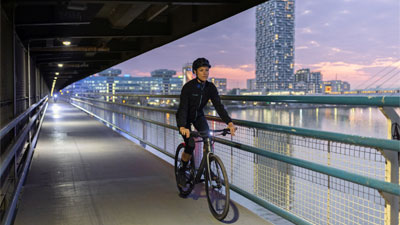 A woman can be seen riding her bike through an underpass, with a large city in the background.