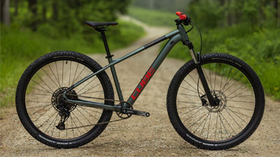 The image shows a gray Cube mountain bike with red details on a gravel path.